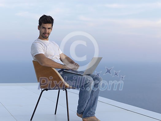 handsome young man relaxing and working on laptop computer at home balcony while looking sunset handsome young man relaxing and working on laptop computer at home balcony while looking sunset
