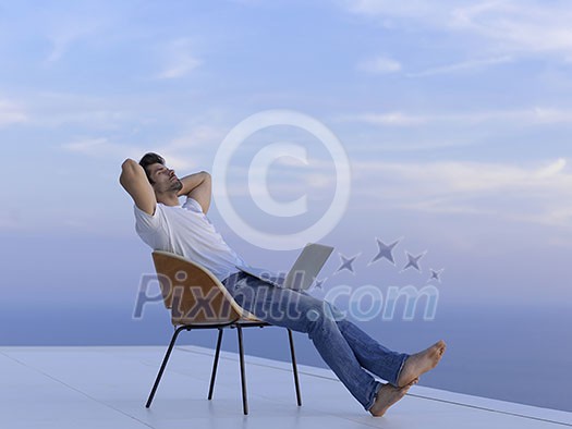 handsome young man relaxing and working on laptop computer at home balcony while looking sunset handsome young man relaxing and working on laptop computer at home balcony while looking sunset