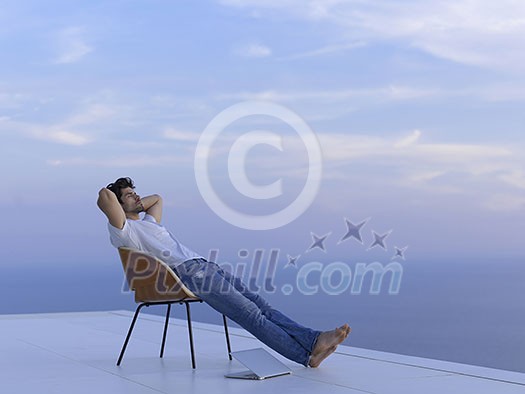 handsome young man relaxing and working on laptop computer at home balcony while looking sunset handsome young man relaxing and working on laptop computer at home balcony while looking sunset