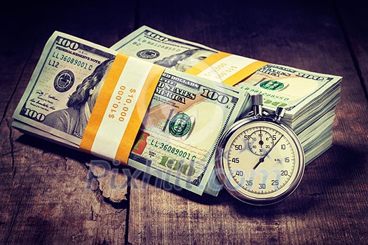 Time is money loan concept background. Vintage retro effect filtered hipster style image of stopwatch and stack of new 100 US dollars 2013 edition banknotes bills bundles on wooden background Time is money loan concept background. Vintage retro effect filtered hipster style image of stopwatch and stack of new 100 US dollars 2013 edition banknotes bills bundles on wooden background