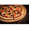 Sliced ham pizza with capsicum and olives on wooden board on table