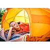 Pretty, young woman camping outdoors, lying in the tent in the morning, using her smart phone