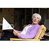 Senior woman reading morning newspaper, sitting in her favorite chair in her living room, looking happy