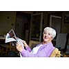 Senior woman reading morning newspaper, sitting in her favorite chair in her living room, looking happy