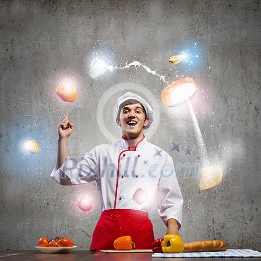 Young cheerful cook and ingredients flying in air Young cheerful cook and ingredients flying in air