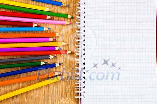 Colored pencils and notepad on wooden table Colored pencils and notepad on wooden table
