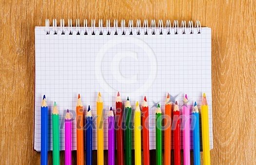 Colored pencils and notepad on wooden table Colored pencils and notepad on wooden table