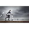 Young cheerful businessman riding scooter against city background
