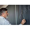 Senior chemistry professor writing on the board while having a chalk and blackboard lecture (shallow DOF; color toned image)