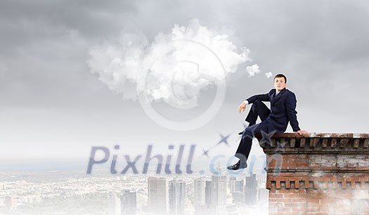 Young businessman sitting on roof of building Young businessman sitting on roof of building