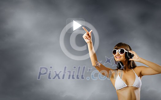 Young attractive girl in bikini wearing headphones touching media icon Young attractive girl in bikini wearing headphones touching media icon