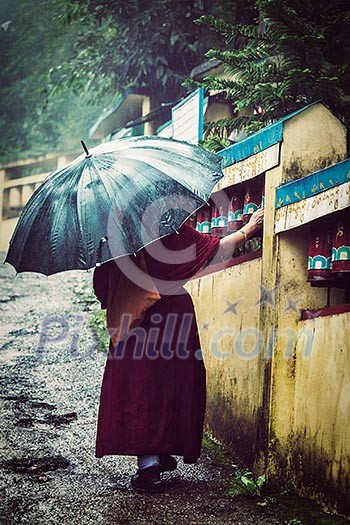 Vintage retro effect filtered hipster style image of Buddhist monk with umbrella spinning prayer wheels on kora around Tsuglagkhang complex in McLeod Ganj, Himachal Pradesh, India. Vintage retro effect filtered hipster style image of Buddhist monk with umbrella spinning prayer wheels on kora around Tsuglagkhang complex in McLeod Ganj, Himachal Pradesh, India.