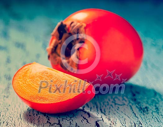 Vintage retro effect filtered hipster style image of fresh ripe persimmon with slice on a blue wooden background Vintage retro effect filtered hipster style image of fresh ripe persimmon with slice on a blue wooden background