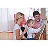 happy young family teach leassons and prepare their son for school while draw on board at home