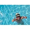 Happy smiling woman with hat and sunglasses  in swimming pool at tropical resort
