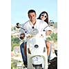 Portrait of happy young love couple on scooter enjoying themselves in a park at summer time