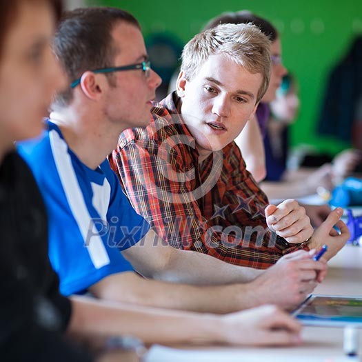 Handsome college student sitting in a classroom full of students during class (color toned image; shallow DOF) Handsome college student sitting in a classroom full of students during class (color toned image; shallow DOF)