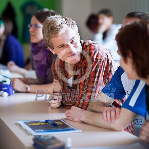 Handsome college student sitting in a classroom full of students during class (color toned image; shallow DOF) Handsome college student sitting in a classroom full of students during class (color toned image; shallow DOF)