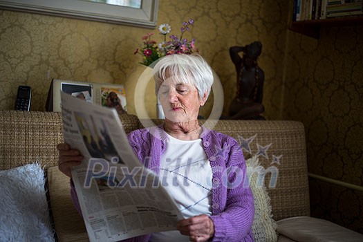 Senior woman reading morning newspaper, sitting in her favorite chair in her living room, looking happy Senior woman reading morning newspaper, sitting in her favorite chair in her living room, looking happy