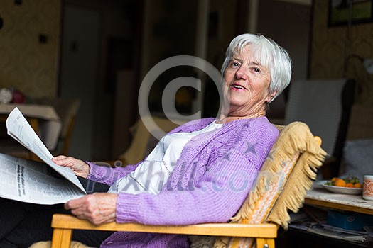 Senior woman reading morning newspaper, sitting in her favorite chair in her living room, looking happy Senior woman reading morning newspaper, sitting in her favorite chair in her living room, looking happy