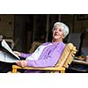 Senior woman reading morning newspaper, sitting in her favorite chair in her living room, looking happy