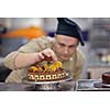 Closeup of a concentrated male pastry chef decorating dessert cake food in the kitchen