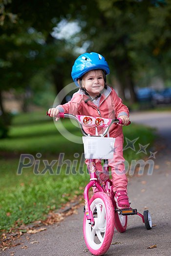 Cute smiling little girl with bicycle and helmet on road in the park Cute smiling little girl with bicycle and helmet on road in the park