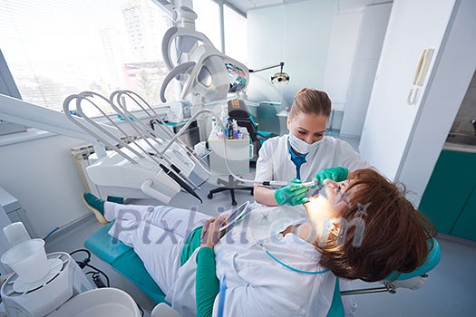 Closeup of a woman patient at the dentist waiting to be checked up with the woman doctor in the background Closeup of a woman patient at the dentist waiting to be checked up with the woman doctor in the background