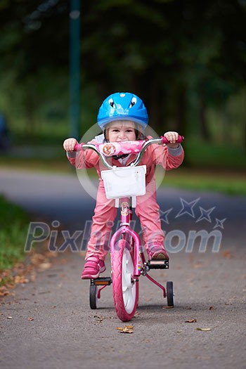 Cute smiling little girl with bicycle and helmet on road in the park Cute smiling little girl with bicycle and helmet on road in the park
