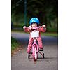 Cute smiling little girl with bicycle and helmet on road in the park