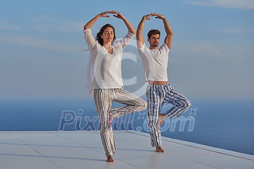 young couple practicing yoga at sunset in modern home terace with ocean and sunset in background young couple practicing yoga at sunset in modern home terace with ocean and sunset in background