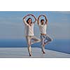 young couple practicing yoga at sunset in modern home terace with ocean and sunset in background