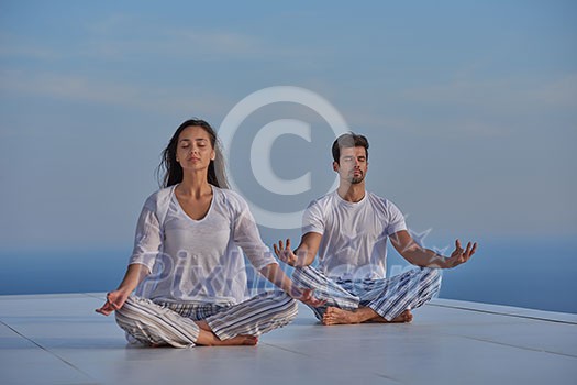 young couple practicing yoga at sunset in modern home terace with ocean and sunset in background