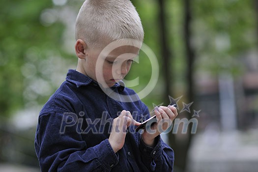 young blonde boy playing videogames outdoor in park young blonde boy playing videogames outdoor in park
