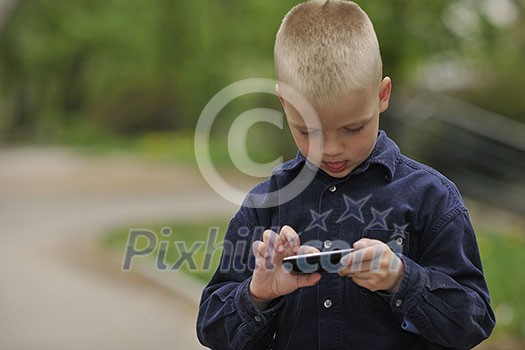 young blonde boy playing videogames outdoor in park young blonde boy playing videogames outdoor in park