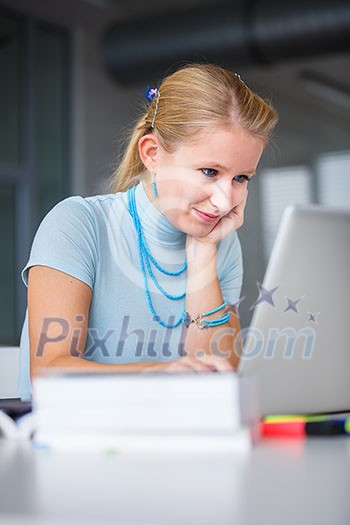 In the library - pretty, female student with books, papers and laptop computer working in a high school library (color toned image) In the library - pretty, female student with books, papers and laptop computer working in a high school library (color toned image)