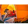 Pretty, young woman camping outdoors, lying in the tent in the morning, using her smart phone