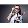 Funny portrait of a young female hairstylist, holding her tools and posing with a comb in front of her eyes ion front of a grey backdrop (color toned image; shallow DOF)