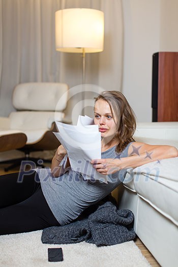 Pretty, young woman going through some paperwork in her lovely living room at night Pretty, young woman going through some paperwork in her lovely living room at night