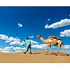 Rajasthan travel background - Indian cameleer (camel driver) with camels in dunes of Thar desert. Jaisalmer, Rajasthan, India