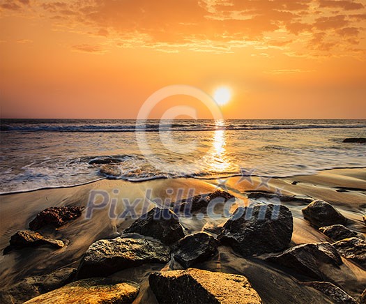 Tropical beach vacation background - waves and rocks on beach on sunset with beautiful cloudscape Tropical beach vacation background - waves and rocks on beach on sunset with beautiful cloudscape
