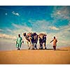 Vintage retro hipster style travel image of Rajasthan travel background - two Indian cameleers (camel drivers) with camels in dunes of Thar desert. Jaisalmer, Rajasthan, India with grunge texture overlaid