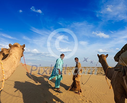 Rajasthan travel background - two indian cameleers (camel drivers) with camels in dunes of Thar desert. Jaisalmer, Rajasthan, India Rajasthan travel background - two indian cameleers (camel drivers) with camels in dunes of Thar desert. Jaisalmer, Rajasthan, India