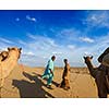 Rajasthan travel background - two indian cameleers (camel drivers) with camels in dunes of Thar desert. Jaisalmer, Rajasthan, India