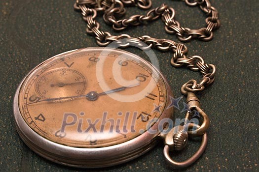 Very old clock with chain lying on rough green surface - shallow depth of field Very old clock with chain lying on rough green surface - shallow depth of field
