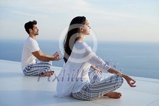 young couple practicing yoga at sunset in modern home terace with ocean and sunset in background young couple practicing yoga at sunset in modern home terace with ocean and sunset in background