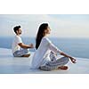 young couple practicing yoga at sunset in modern home terace with ocean and sunset in background