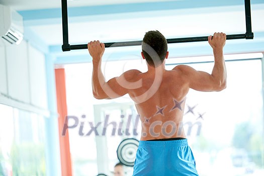 handsome young man in fitness gym lifting up and hanging while working on hands and back muscles handsome young man in fitness gym lifting up and hanging while working on hands and back muscles
