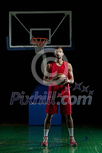 Basketball player portrait on basketball court holding ball with black isolated background Basketball player portrait on basketball court holding ball with black isolated background