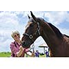 happy woman in sunglasses sitting on horse farm animal outdoors with blue sky in background